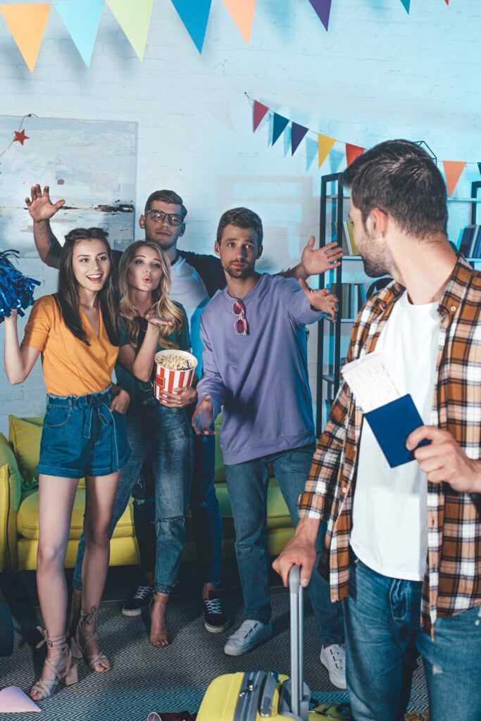 young man with passport and suitcase looking at friends at farewell party